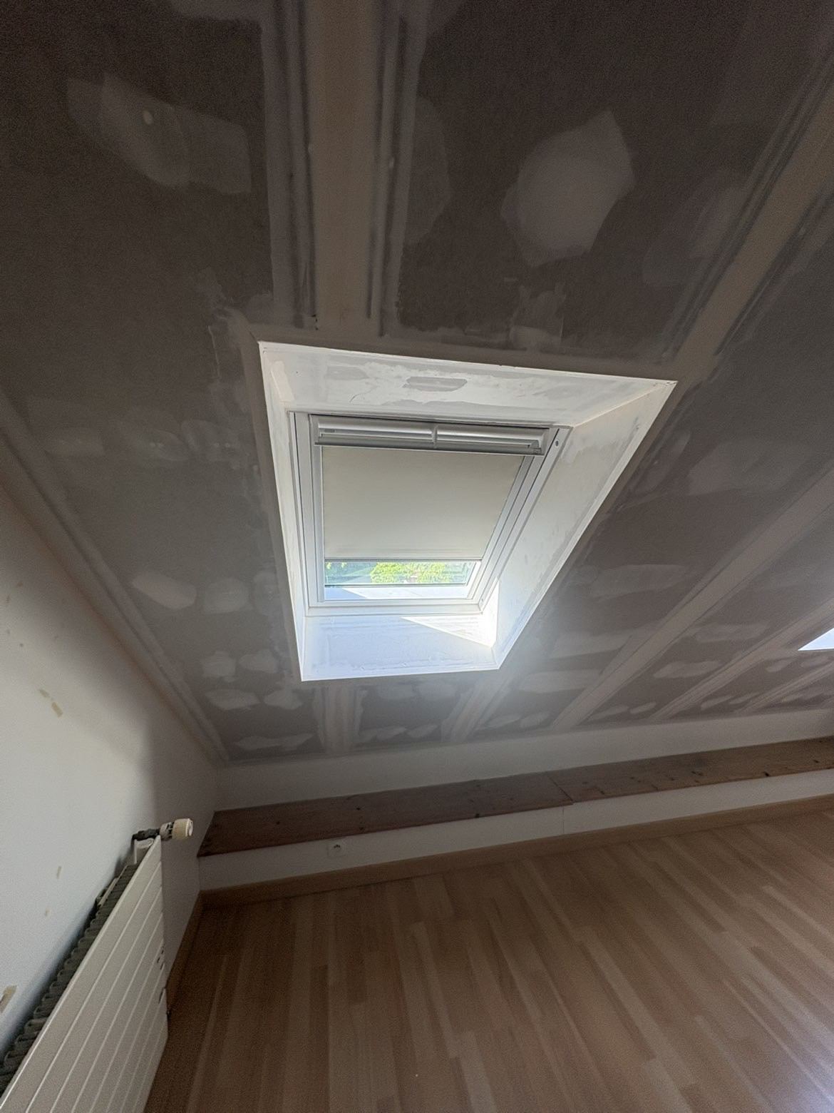 Combles en cours d'aménagement : plaques de plâtre jointoyées, parquet neuf et fenêtre de toit avec store
