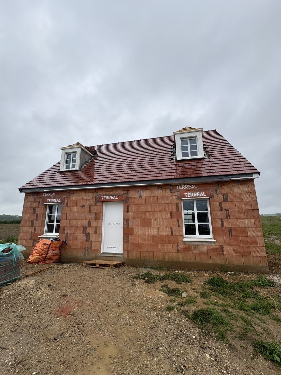 Maison neuve en briques avec porte, fenêtres et lucarnes blanches fraîchement posées