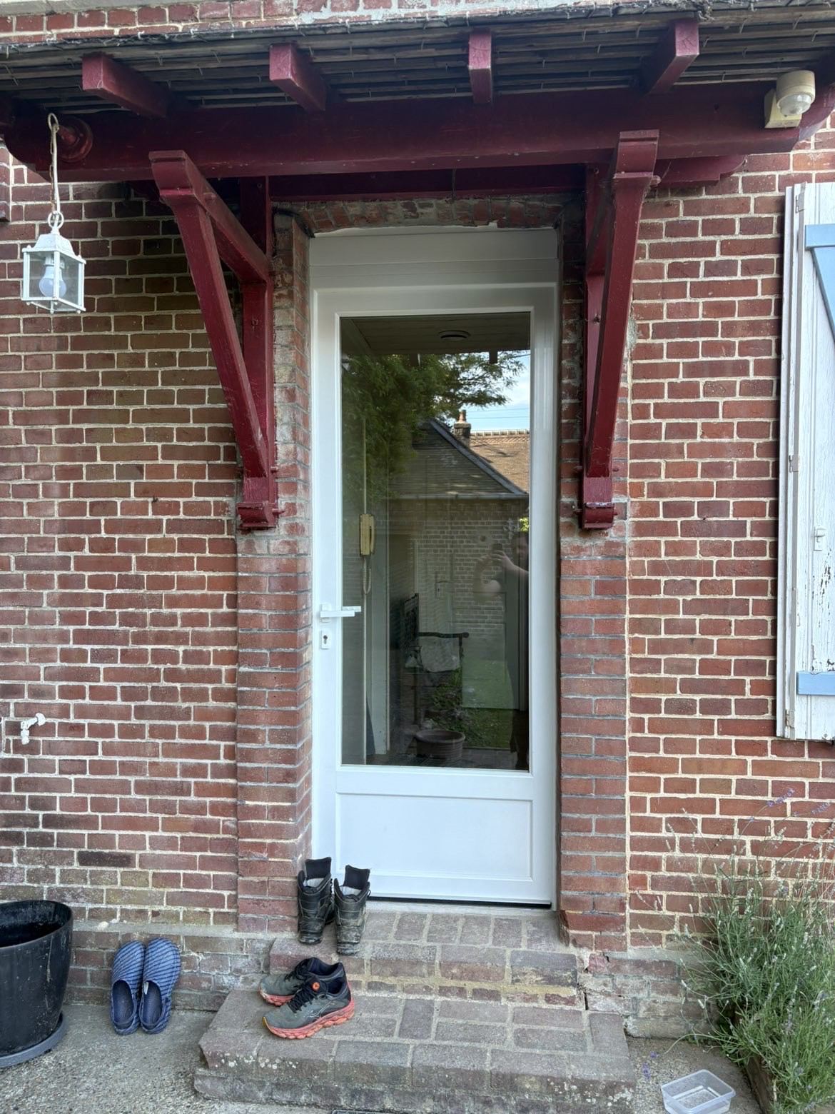 Porte d'entrée vitrée blanche posée sur une maison en briques rouges, sous son auvent d'origine