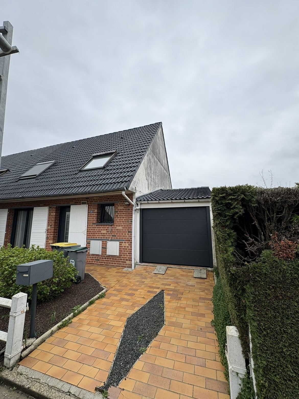 Porte de garage sectionnelle gris anthracite posée sur un garage attenant à une maison en briques