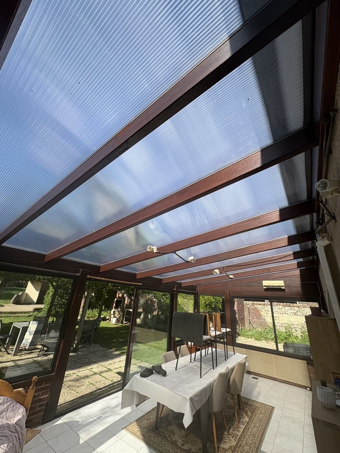 Véranda à ossature bois et toiture translucide rénovée par JM RENOVATION, ouverte sur le jardin